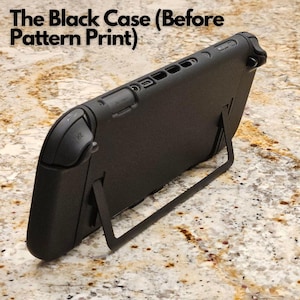 May include: A black gaming console case with a built-in stand. The case is shown at an angle, revealing the side with buttons and ports. The text "The Black Case (Before Pattern Print)" is at the top of the image. The case is on a speckled surface.