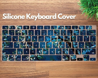 May include: A silicone keyboard cover with a floral design. The cover features a dark blue background with white and light blue floral accents. The text "Silicone Keyboard Cover" is displayed at the top.