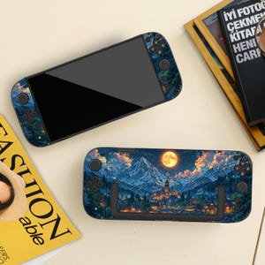 May include: Two handheld gaming consoles with decorative skins. One console features a landscape design with a full moon, mountains, and a town. The other console has a forest design. The consoles are black with buttons.