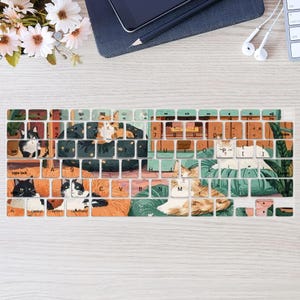 Könnte beinhalten: Eine Tastaturabdeckung mit einem farbenfrohen Design, das Katzen zeigt, die auf einem Sofa und Kissen liegen. Die Abdeckung hat einen hellbraunen Hintergrund mit grünen, blauen und orangefarbenen Akzenten. Die Tasten sind mit Buchstaben und Zahlen beschriftet.