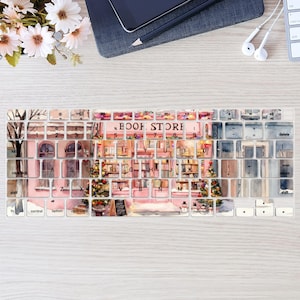 Könnte beinhalten: Eine Tastaturabdeckung mit einem Aquarelldesign, das eine Buchhandlung darstellt. Die Tasten sind mit Bildern von Bücherregalen, Fenstern und Weihnachtsbäumen verziert. Der Text "BOOK STORE" ist oben sichtbar.