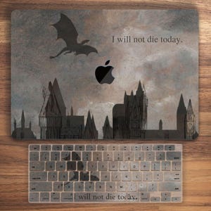 May include: A laptop skin with a dark gray and brown background featuring a silhouette of a dragon flying over a cityscape. The text "I will not die today." is printed on the skin. The skin is designed to fit a MacBook.