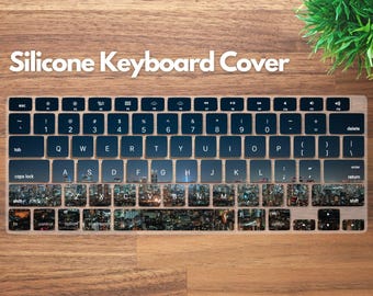 May include: A silicone keyboard cover with a cityscape design. The cover features a full keyboard layout with black keys and white lettering. The cityscape design is visible on the keys. The words "Silicone Keyboard Cover" are at the top.
