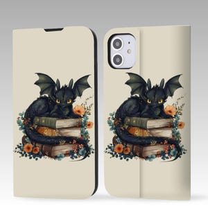 May include: A phone case featuring a black dragon illustration. The dragon is perched atop a stack of books, surrounded by flowers. The case has a cream-colored background and a black border.