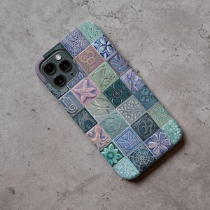 Puede incluir: Funda de teléfono inteligente con diseño de mosaico. La funda presenta imágenes en relieve con temática marina, como una estrella de mar, un cangrejo y flores, en tonos azules, verdes y morados. La funda está diseñada para un teléfono inteligente.