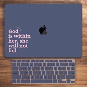 Könnte beinhalten: Ein blauer Laptop mit einem rosafarbenen Zitat, das lautet "Psalm 46:5 Gott ist in ihr, sie wird nicht versagen". Der Laptop ist geschlossen und hat ein schwarzes Apple-Logo. Unter dem Laptop befindet sich eine blaue Tastatur.