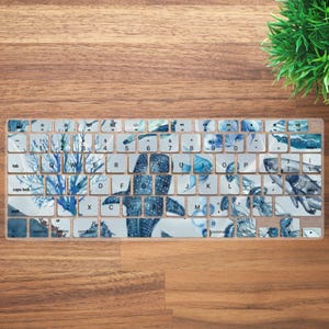 May include: A keyboard cover with a marine life design. The keys feature a blue and white watercolor pattern with images of coral, fish, and sharks. The cover is designed to fit a standard keyboard layout.