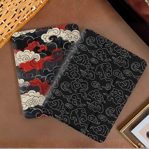 May include: Two tablet cases with cloud designs. One case features a black background with red, white, and black clouds. The other case has a black background with white cloud outlines. The cases are on a brown surface.
