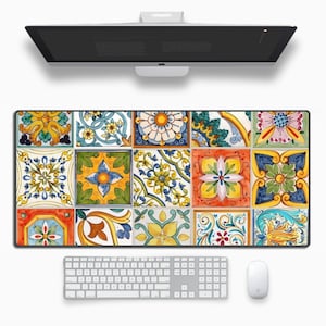 May include: A desk mat with a vibrant, tiled design showcasing floral and geometric patterns in blue, yellow, orange, and green. A white keyboard and mouse are positioned below the mat, with a computer monitor above.