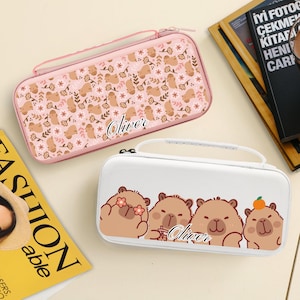 Puede incluir: Dos estuches rectangulares, uno rosa y otro blanco, con cierres de cremallera y asas. El estuche rosa presenta un estampado de osos marrones y flores, con el nombre "Oliver" en cursiva. El estuche blanco tiene un diseño de cuatro osos de dibujos animados.