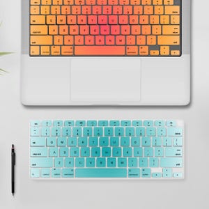 May include: A laptop and a separate keyboard with colourful keycaps. The laptop keyboard has orange and yellow keycaps, while the separate keyboard has blue and teal keycaps. A black pen is on the left.