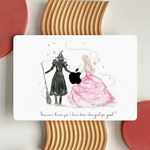 May include: A white background with a watercolor illustration of two women, one in a black dress and a green witch's hat, and the other in a pink dress. The women are walking away from each other, and there is a black apple logo between them. The text "Because I knew you, I have been changed for good" is written below the illustration.