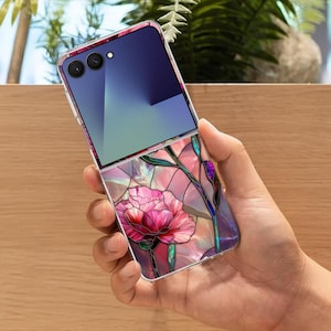 May include: A smartphone case with a floral stained glass design. The case features a large pink flower with green stems and leaves, set against a backdrop of pink, purple, and blue hues. The top portion of the phone is a gradient of blue.