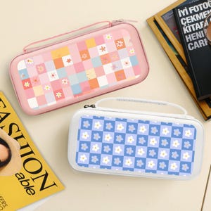 Peut inclure: Deux étuis rectangulaires avec poignées. L'un est rose avec un motif patchwork de carrés et de fleurs. L'autre est blanc avec un motif floral bleu et blanc. Les deux étuis ont des fermetures éclair.