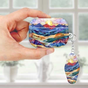 May include: A colorful AirPod case and matching keychain featuring a stained-glass style landscape with a sun, mountains, and flowing water. The case is held in a hand, showcasing the design's vibrant hues of blue, orange, and purple.