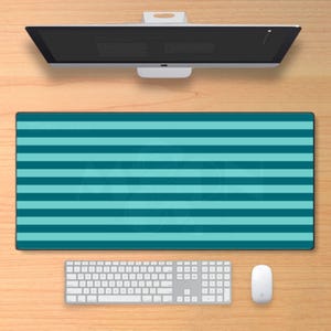 May include: A rectangular desk mat featuring a repeating horizontal striped pattern in alternating shades of teal and light blue. The mat is positioned on a wooden surface below a computer monitor, a white keyboard, and a white computer mouse.