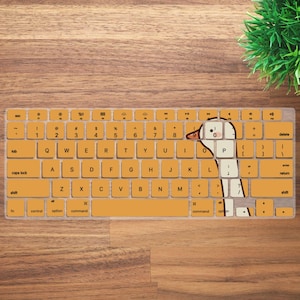 May include: A keyboard cover with a cartoon goose design. The cover is a mustard yellow color with white keys and a goose illustration. The keyboard layout is visible, with letters, numbers, and function keys.