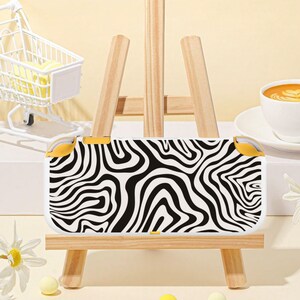 May include: A handheld gaming console featuring a white shell with a black wavy, abstract zebra-like pattern across the front. The device includes yellow accent buttons on the top corners and a small yellow button on the bottom edge.