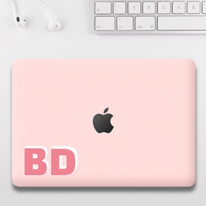 May include: A pink laptop computer with a black Apple logo and a pink sticker that says "BD" on the lid.