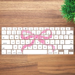 Pode incluir: Um teclado branco com uma sobreposição de design de laço rosa. O teclado possui teclas padrão, incluindo letras, números e teclas de função. O design do laço é centralizado e cobre várias teclas.