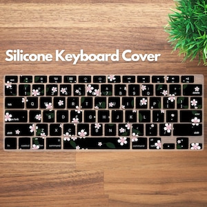 May include: A black silicone keyboard cover with a floral design. The cover features white and pink cherry blossom flowers and green leaves. The text "Silicone Keyboard Cover" is at the top.