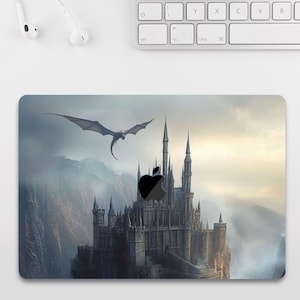 Può includere: Una skin per laptop di colore grigio scuro con una scena fantasy di un drago nero che vola sopra un grande castello di pietra grigia con un cielo nuvoloso sullo sfondo. Il logo Apple è visibile sul castello.