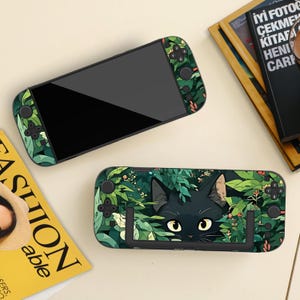 Peut inclure: Deux coques noires pour console de jeu portable. L'une est verte avec un motif de feuilles. L'autre est verte avec un chat noir qui regarde derrière des feuilles. Les coques ont des boutons noirs et un écran noir.