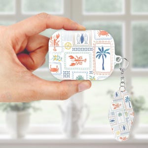 May include: White AirPod case with a keychain, featuring a repeating pattern of sea-themed illustrations. The design includes images of lobsters, fish, palm trees, and crabs in orange, blue, and green. The case is held by a hand.