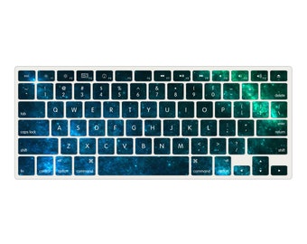 May include: A keyboard cover with a galaxy print in shades of blue and green. The cover features a standard keyboard layout with keys labeled for a Mac computer.