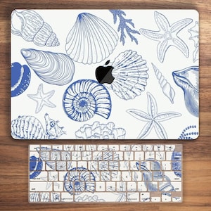 Op de afbeelding: Een witte laptop-skin met een blauw schelp- en zeesterrenontwerp. De skin is ontworpen om te passen op een MacBook-laptop.