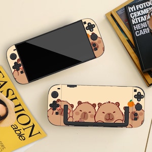 Puede incluir: Dos consolas Nintendo Switch beige con un diseño de oso de dibujos animados. Las consolas tienen pantallas negras y botones negros. Una consola está en posición vertical y la otra está plana. El diseño presenta osos marrones con bebidas y una naranja.