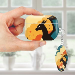 May include: A yellow and orange AirPod case with a black dragon graphic and a matching keychain. The design features a dragon silhouette against a sunset-like background with orange and teal accents. The case has a silver metal loop for the keychain.