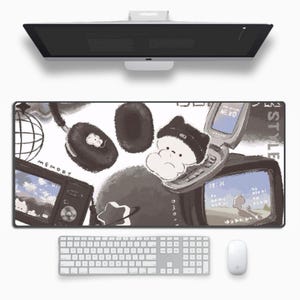 May include: A long, rectangular mouse mat featuring a monochrome illustration with a cartoon character, headphones, a retro TV, and a flip phone. The word "MEMORY" is visible. A white keyboard and mouse are below.