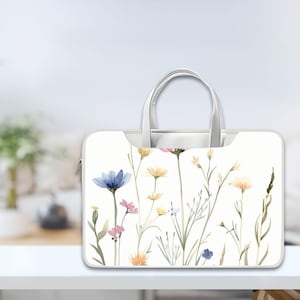 May include: White laptop bag with a floral design featuring blue, yellow, and pink flowers. The bag has a zipper and a handle.