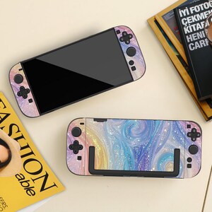 May include: Two Nintendo Switch consoles with colorful, swirling designs in shades of pink, blue, and yellow. The controllers and console have a matching pattern. The screen is black.