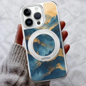 Könnte beinhalten: Eine transparente Handyhülle mit einem Berglandschaftsdesign in Blau-, Gold- und Orangetönen. Die Hülle hat einen silbernen Ring auf der Rückseite. Die Handyhülle ist für ein Smartphone konzipiert.