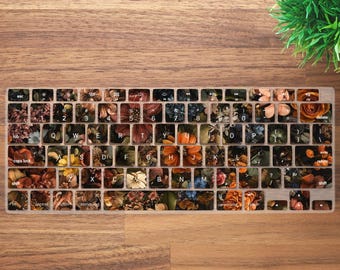 May include: A keyboard with a floral design overlay. The keys are adorned with various flower images in shades of orange, brown, and green. The keyboard sits on a wooden surface, with a small green plant in the upper right corner.