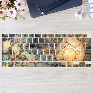 以下が含まれることがあります： 青、金、クリーム色を基調としたステンドグラスデザインのキーボードカバー。キーには文字と数字が印字されています。標準的なキーボードレイアウトに合うように設計されています。