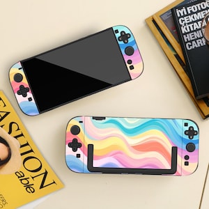 May include: Two colorful game console cases with a rainbow wave pattern. The cases have black screens and control buttons. One case is open, and the other is closed. The cases are on a light-colored surface.