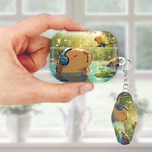 May include: A light brown AirPod case and matching keychain featuring a cartoon capybara wearing headphones in a pond. The case and keychain have a green and blue background with a parrot perched on a branch.