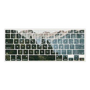 May include: A keyboard cover with a mountain and forest scene printed on it. The keys are visible through the image, and the cover is designed to fit a standard keyboard.
