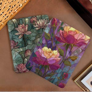 Puede incluir: Dos fundas rectangulares para lector electrónico con patrones florales estilo vidriera. Una funda muestra nenúfares rosas sobre hojas verdes, mientras que la otra presenta grandes peonías magenta y amarillas con hojas verdes y contornos.