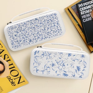 May include: Two white carrying cases with blue floral patterns. Each case has a white handle and zipper. The cases are rectangular and appear to be made of a hard material. The floral design is a repeating pattern of leaves and flowers.