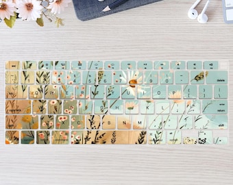 May include: A keyboard cover with a floral design featuring a light blue background with white, yellow, and brown flowers. The keyboard cover has keys labeled with letters, numbers, and symbols.