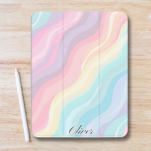 Könnte beinhalten: Eine pastellfarbene Tablet-Hülle mit einem wellenförmigen Muster in Rosa, Lila, Gelb und Blau. Das Wort "Oliver" ist kursiv geschrieben. Ein weißer Stift liegt neben der Hülle.