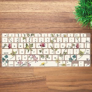 May include: A white keyboard with a floral design. The keys have a clear protective layer with a floral pattern printed on it. The keyboard has a standard layout with keys for letters, numbers, punctuation, and function keys.