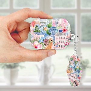 May include: A square, patterned case for wireless earbuds and a matching keychain. The design features a collage of watercolor illustrations, including a golden retriever, flowers, buildings, and citrus fruits. The case is held in a hand.