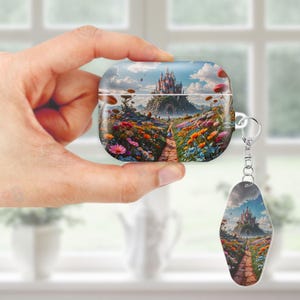 May include: A clear AirPods case and matching keychain featuring a colorful fantasy landscape with a castle, path, and vibrant flowers. The case is held in a hand, showcasing the design's details and the keychain's similar artwork.