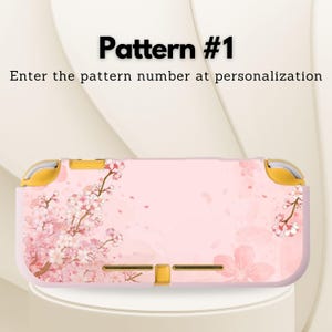 May include: Pink and white floral patterned case for a handheld gaming device. The case features a cherry blossom design with the text "Pattern #1" and "Enter the pattern number at personalization". The case has gold accents.