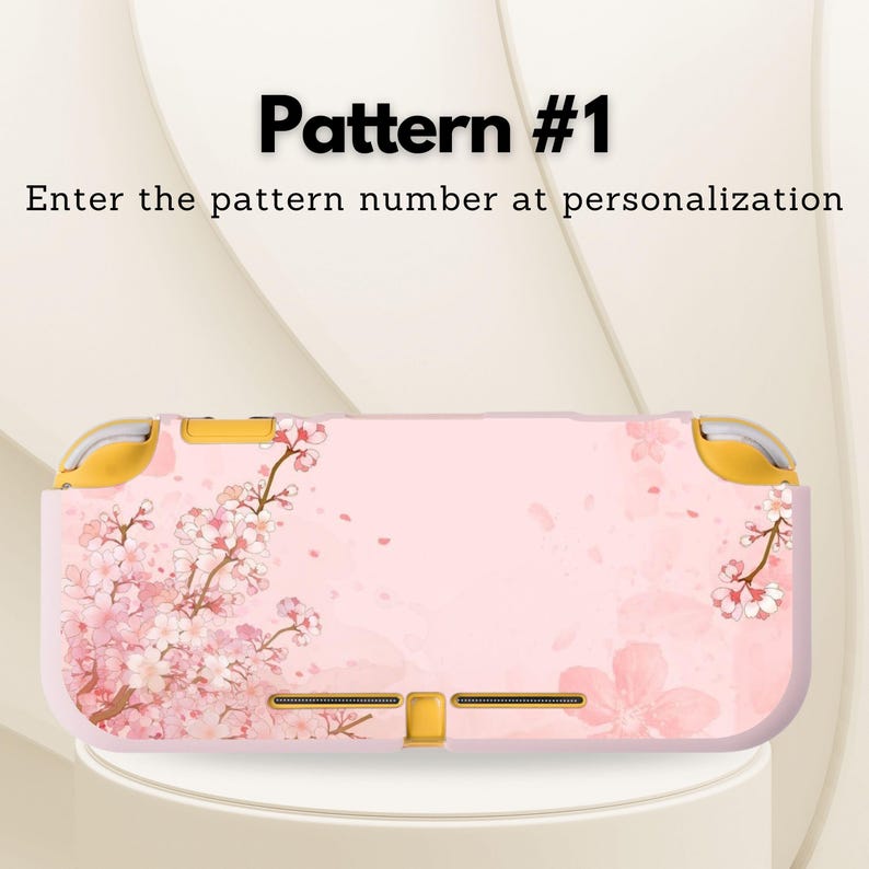 May include: Pink and white floral patterned case for a handheld gaming device. The case features a cherry blossom design with the text "Pattern #1" and "Enter the pattern number at personalization". The case has gold accents.